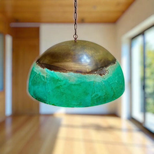 Green and gold pendant light hanging in a room with wooden floor and window.