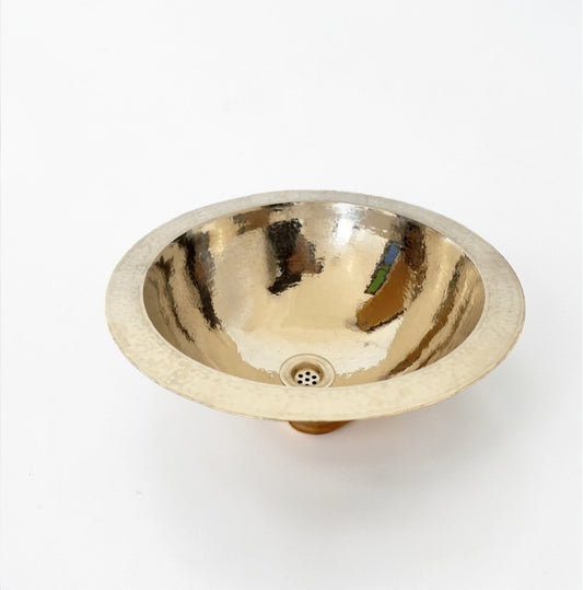 Handcrafted hammered brass drop-in bathroom sink with polished gold finish on marble countertop