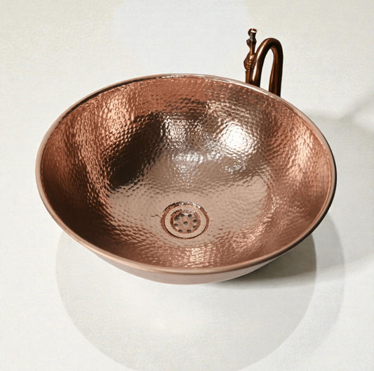 Coppera Studio hammered copper vessel sink with a rounded bowl shape and a drain.